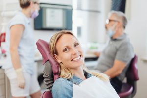 smiling woman sitting in a dental chair while dental team has conversation behind her
