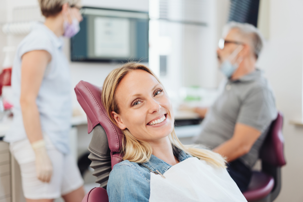 smiling woman sitting in a dental chair while dental team has conversation behind her