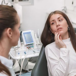 patient holding jaw in discomfort and speaking to dentist